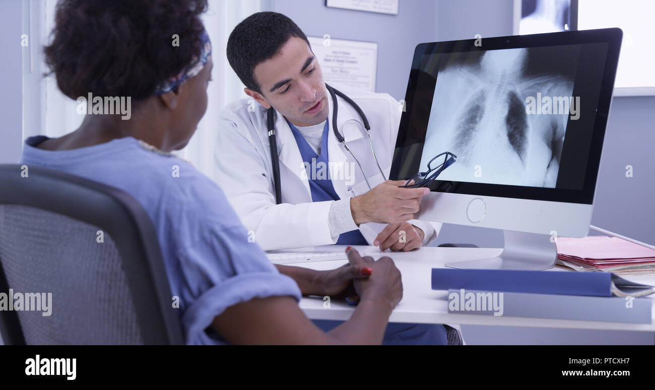 Senior black woman listening to young latino MD as he reviews her x-ray Stock Photo