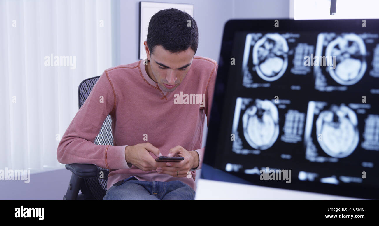 Patient ct-scans on computer while he uses smartphone to send text messages Stock Photo