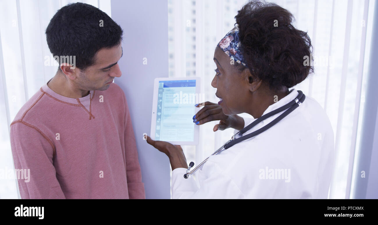 Senior African MD showing male latino patient different health plans on tablet Stock Photo