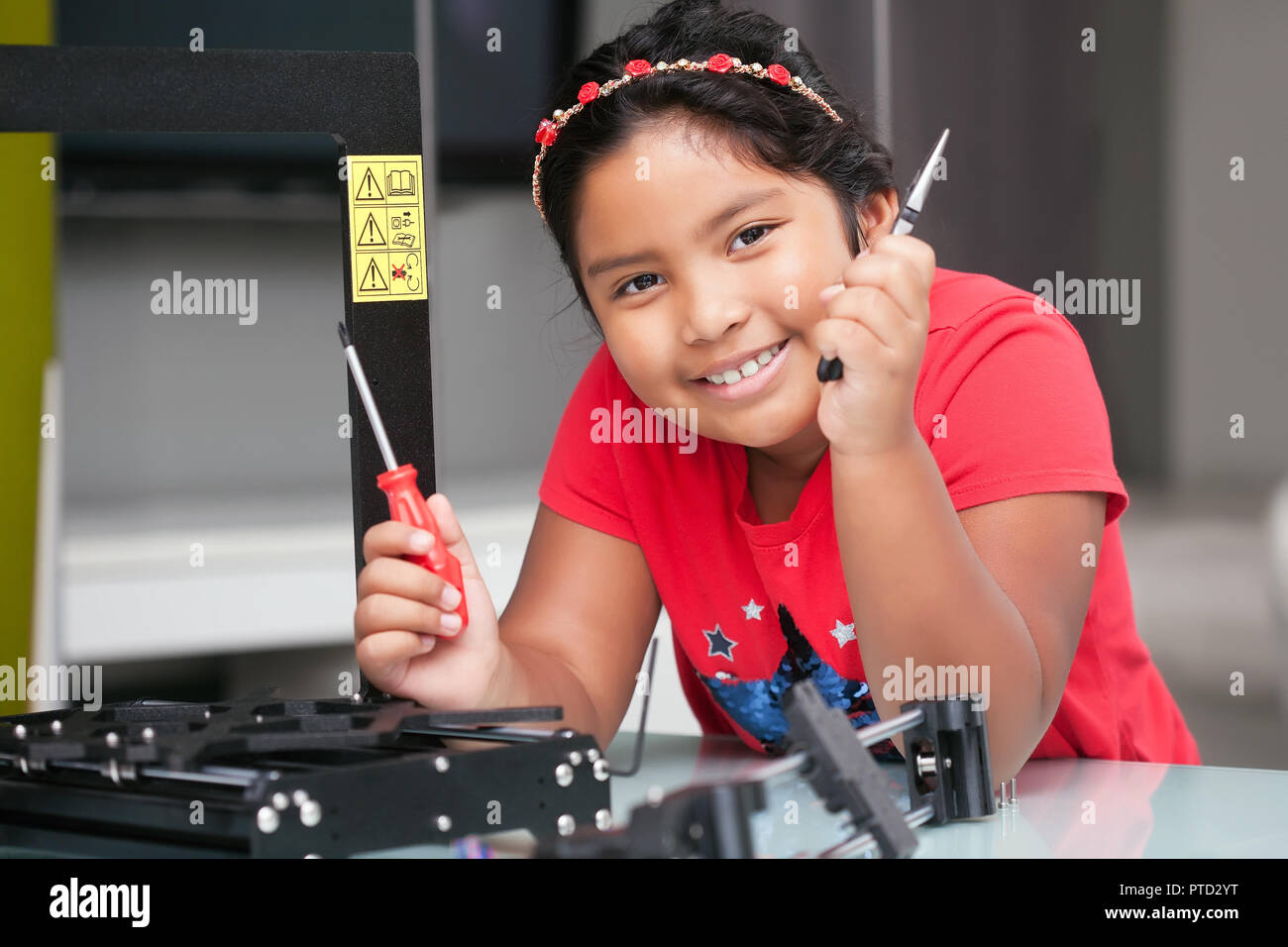 Smart 8 year old girl with tools in hand, ready to assemble a 3D printer with a positive attitude Stock Photo