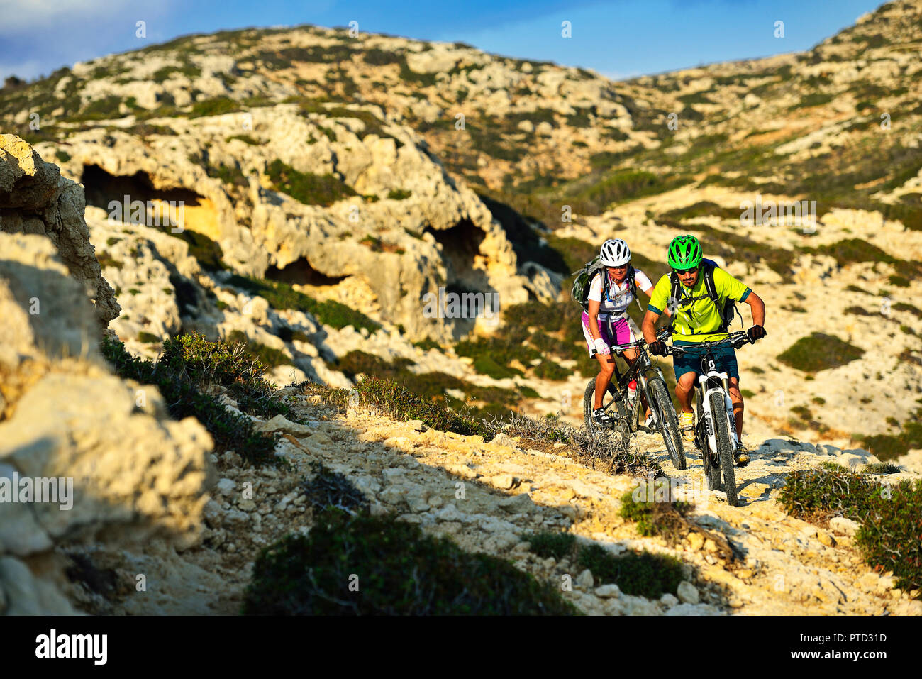 Two mountain bikers cycle in rocky terrain, Red Beach, Matala, Crete, Greece Stock Photo