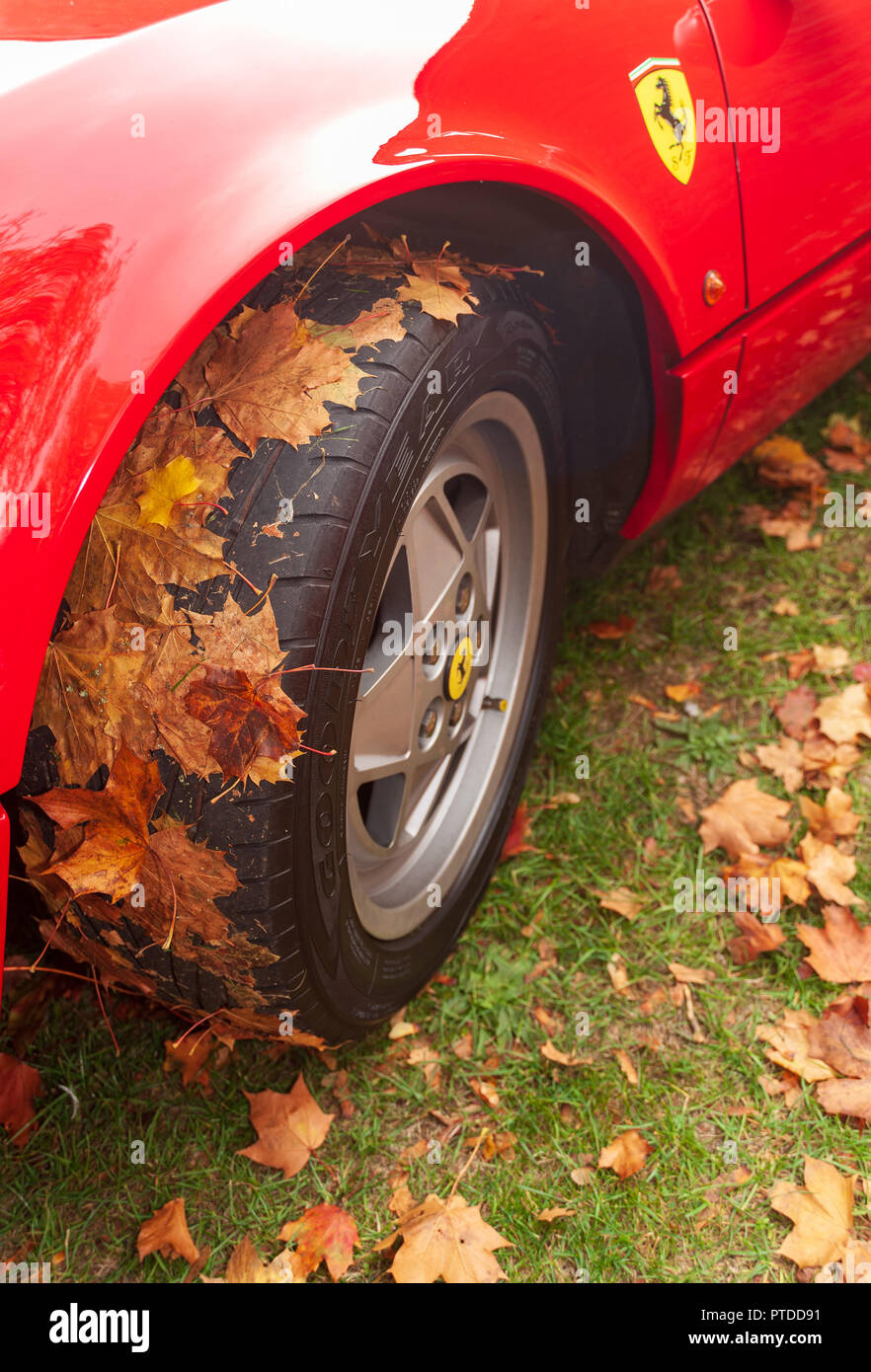 Ferrari in Autumn, close-up of the front wheel  of a red Ferrari, with autumn leaves sticking to the tyre Stock Photo