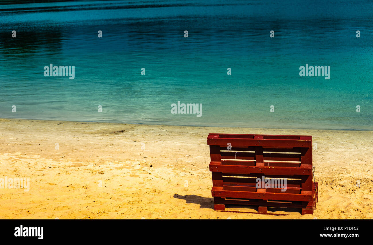 Unreal picture of the end of summer at a lake with an empty beach and a deck chair made of europallets. Stock Photo