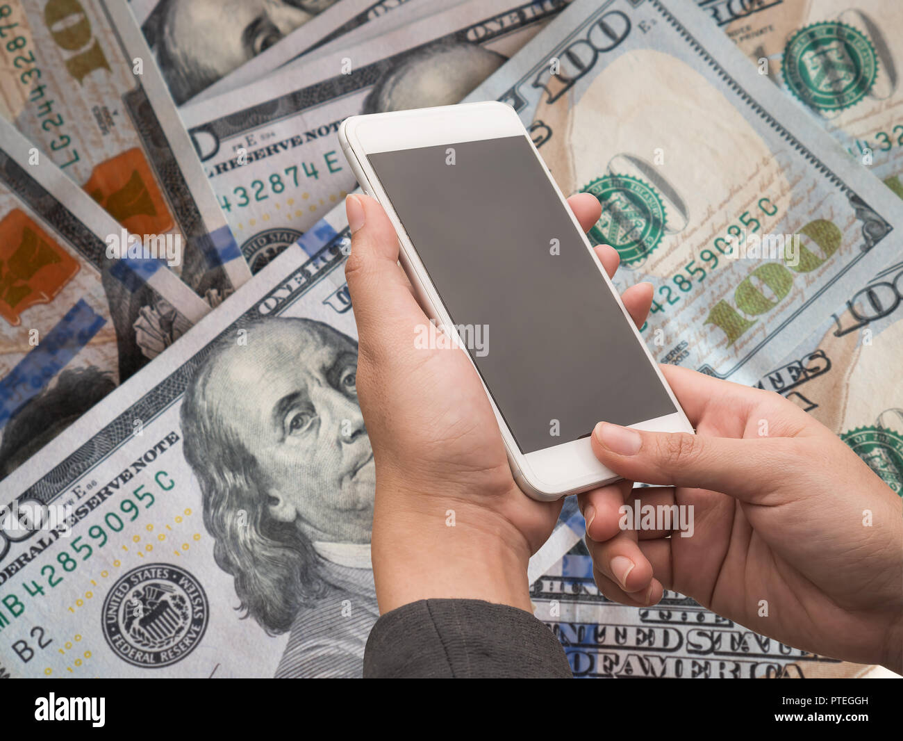 Woman holding white smart phone with blank desktop screen on blur dollars money background. Stock Photo