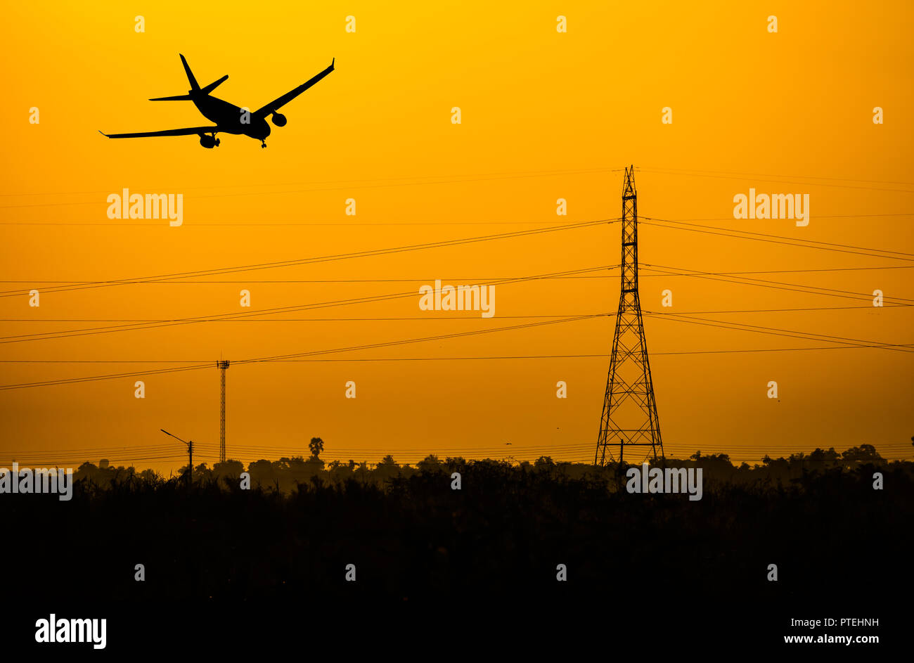Airplane flying over the electtric pole at sunset. Stock Photo
