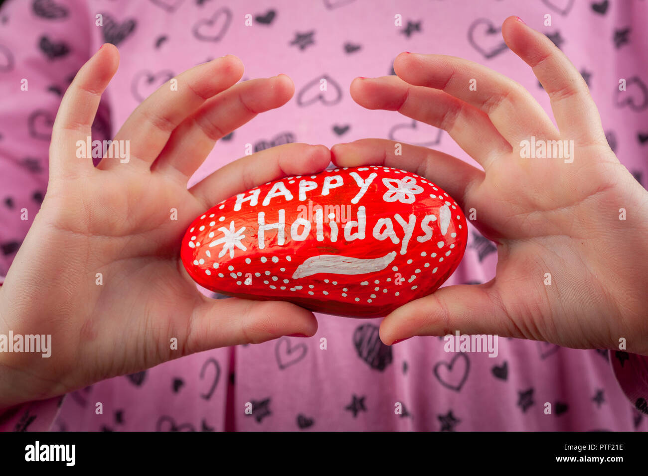 Girl showing red painted rock - Happy Holidays hand lettering greetings closeup Stock Photo