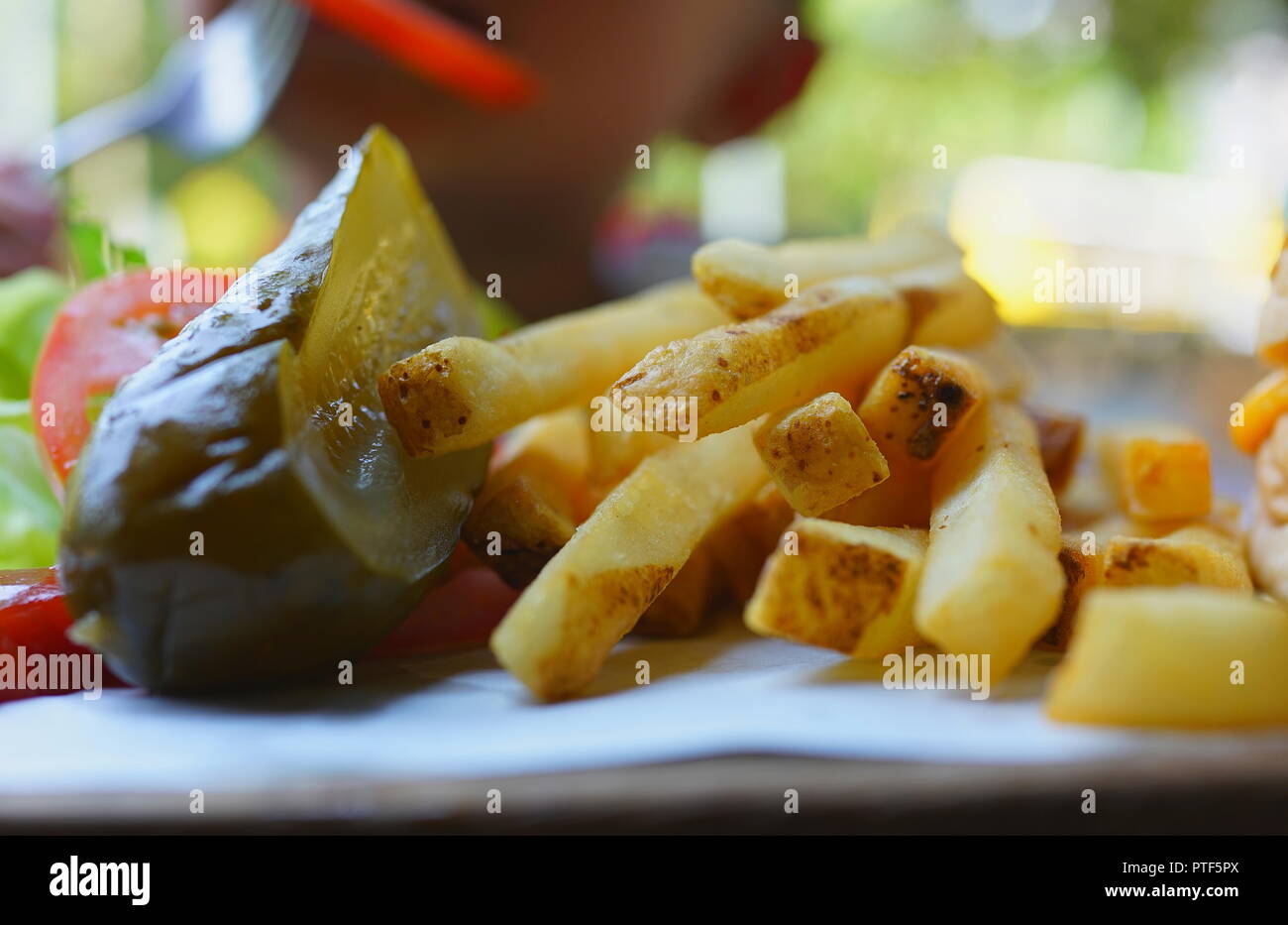 Closeup of pickle and french fries on plate in restaurant outdoor
