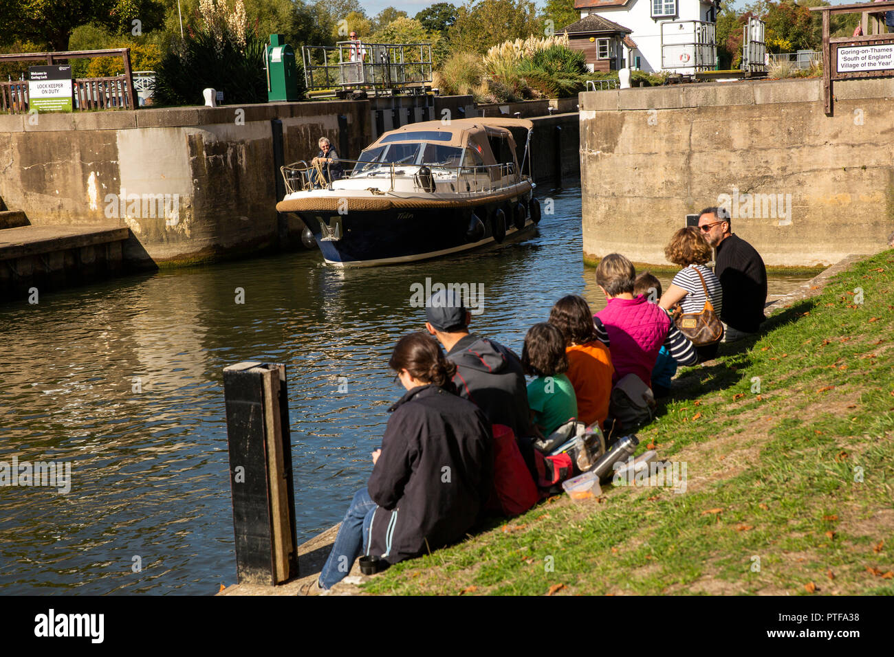 England, Berkshire, Goring on Thames, visitors sat on riverbank in sunshine watching boat leave River Thames locks Stock Photo