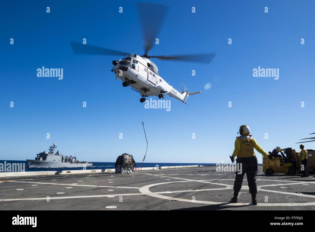 CORAL SEA (July 21, 2017) Aviation Boatswain’s Mate (Handling) 3rd Class Julia Valles, from Mesa, Ariz., directs a SA-330J Puma helicopter, assigned to the Military Sealift Command dry cargo and ammunition ship USNS Richard E. Byrd (T-AKE 4), to drop cargo on the flight deck of the amphibious transport dock USS Green Bay (LPD 20) with the amphibious dock landing USS Ashland (LSD 48) in the distance during a vertical replenishment as a part of Talisman Saber 17. Talisman Saber is a biennial U.S.-Australia bilateral exercise held off the coast of Australia meant to achieve interoperability and s Stock Photo