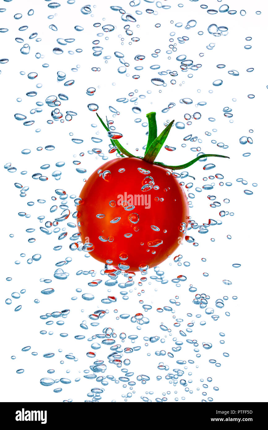 Little cherry tomato splashing into water with air bubbles Stock Photo
