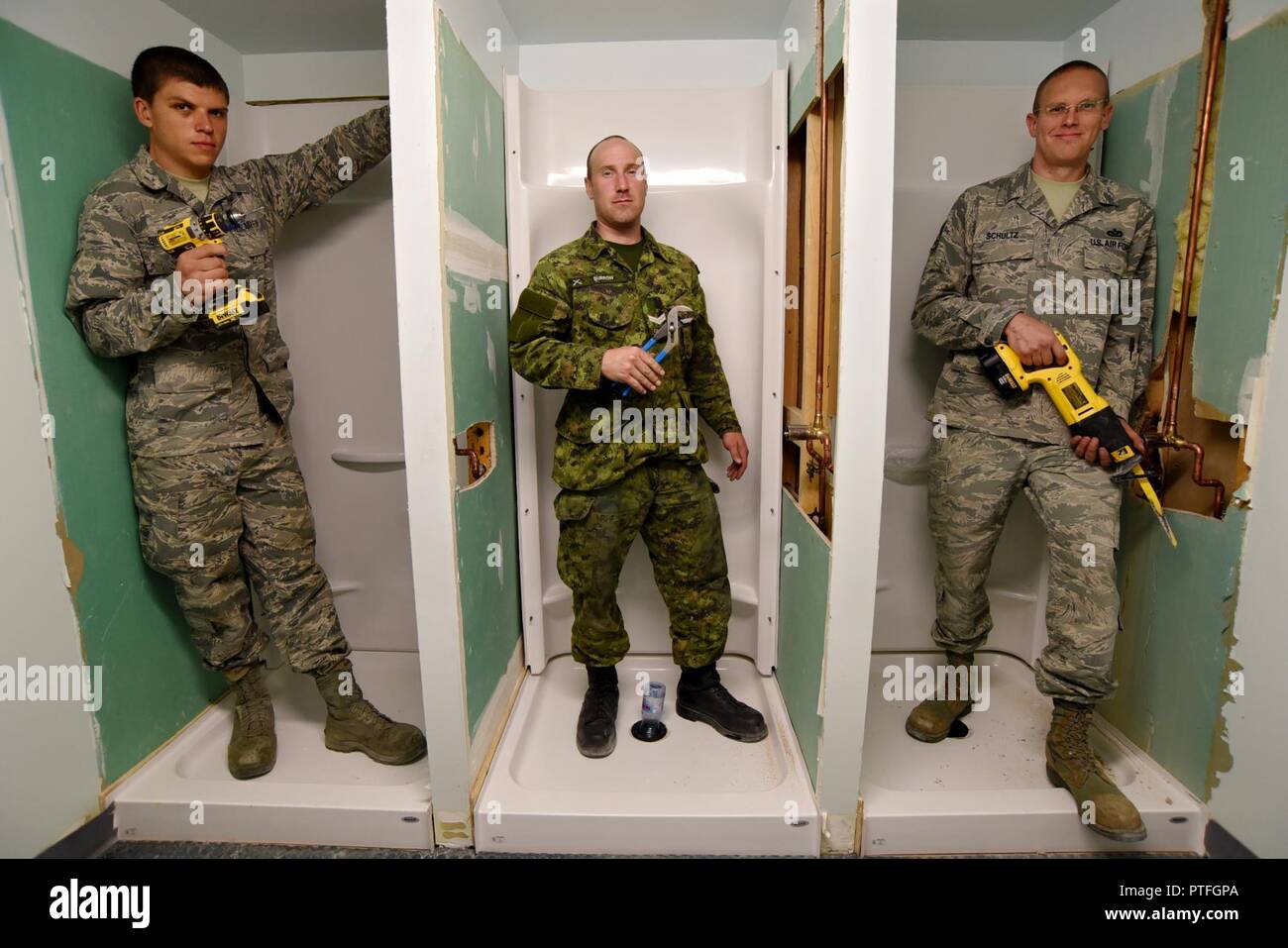 Oregon Air National Guard Staff Sgt. Benjamin Schultz (right), along with Airman 1st Class Joshua Bietschek (left), and Canadian Armed Forces (CAF) Corporal Kyle Burrow (center) pause momentarily for a photograph together as they work on various tasks to rebuild three showers at the military personnel building in Yellowknife, Northwest Territories, Canada, July 21, 2017. The Oregon Airmen are also collaborating with Canadian Armed Forces members from Cold Lake, Alberta, who are also deployed to Yellowknife for training. Stock Photo