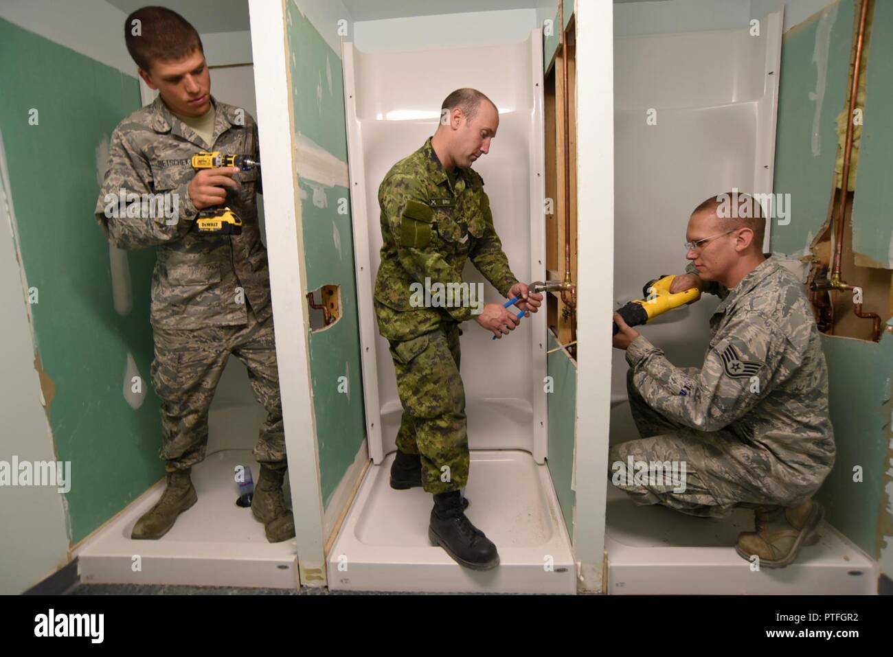Oregon Air National Guard Staff Sgt. Benjamin Schultz (right), along with Airman 1st Class Joshua Bietschek (left), and Canadian Armed Forces (CAF) Corporal Kyle Burrow (center) work on various tasks to rebuild three showers at the military personnel building in Yellowknife, Northwest Territories, Canada, July 21, 2017. The Oregon Airmen are also collaborating with Canadian Armed Forces members from Cold Lake, Alberta, who are also deployed to Yellowknife for training. Stock Photo