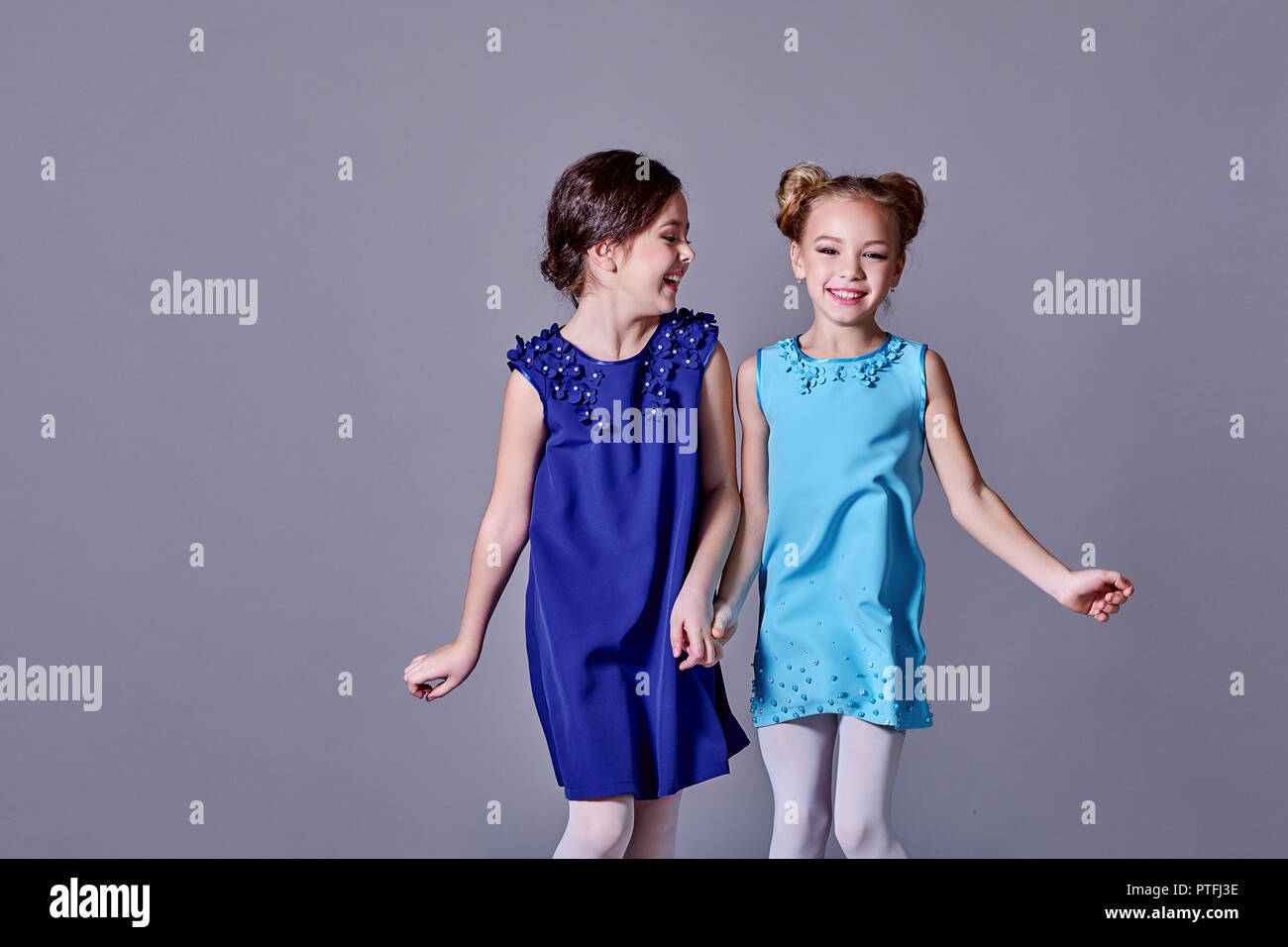 Two 2 little girls having fun in beautiful elegant dresses.Girlfriends fashion model children smile posing studio for catalog designer clothes. Classic lady style for kids, teens. copy space. Stock Photo