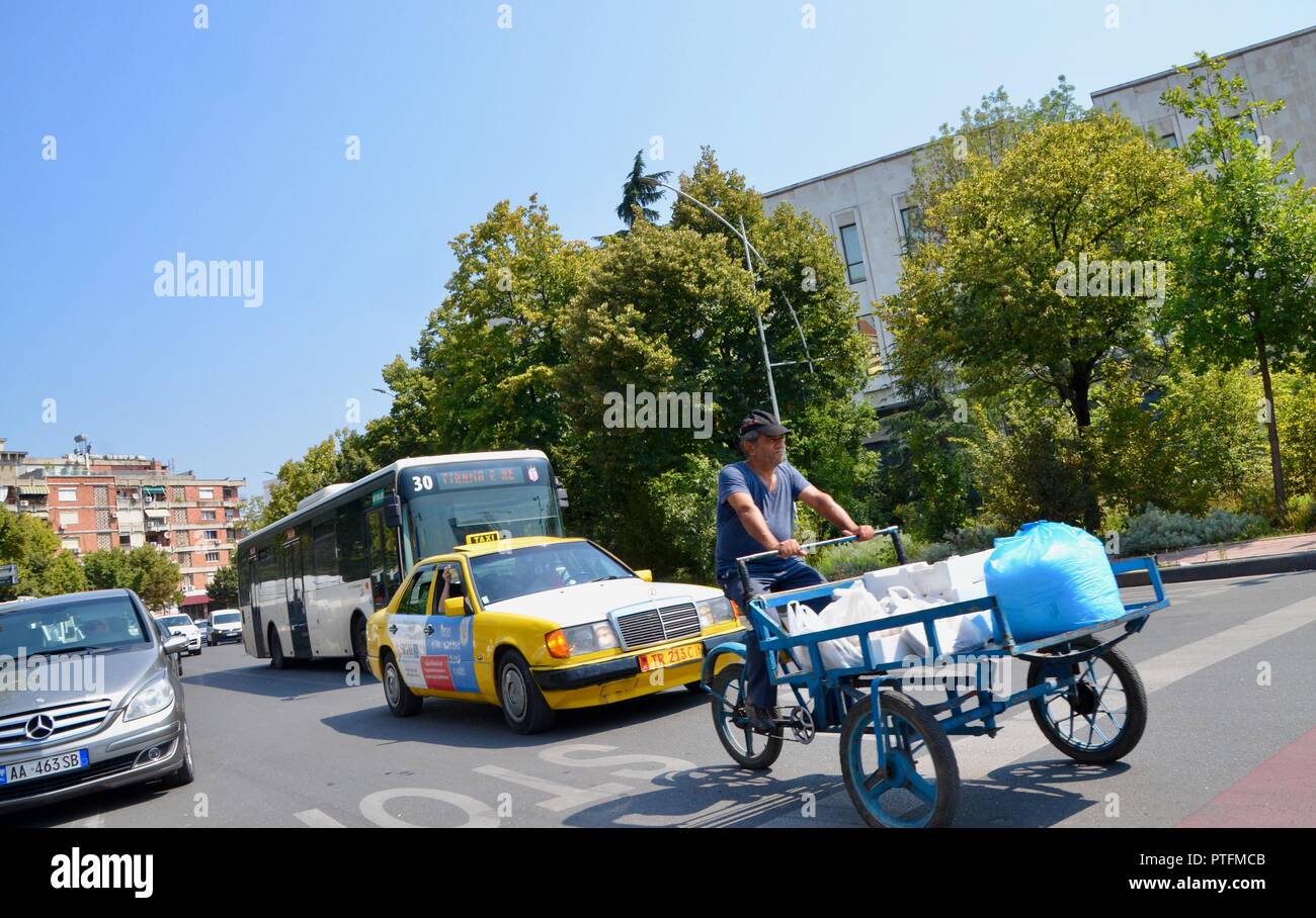 a man on a flatbed tricycle with a taxi and a bus mass by tirana's National History Museum albania Stock Photo