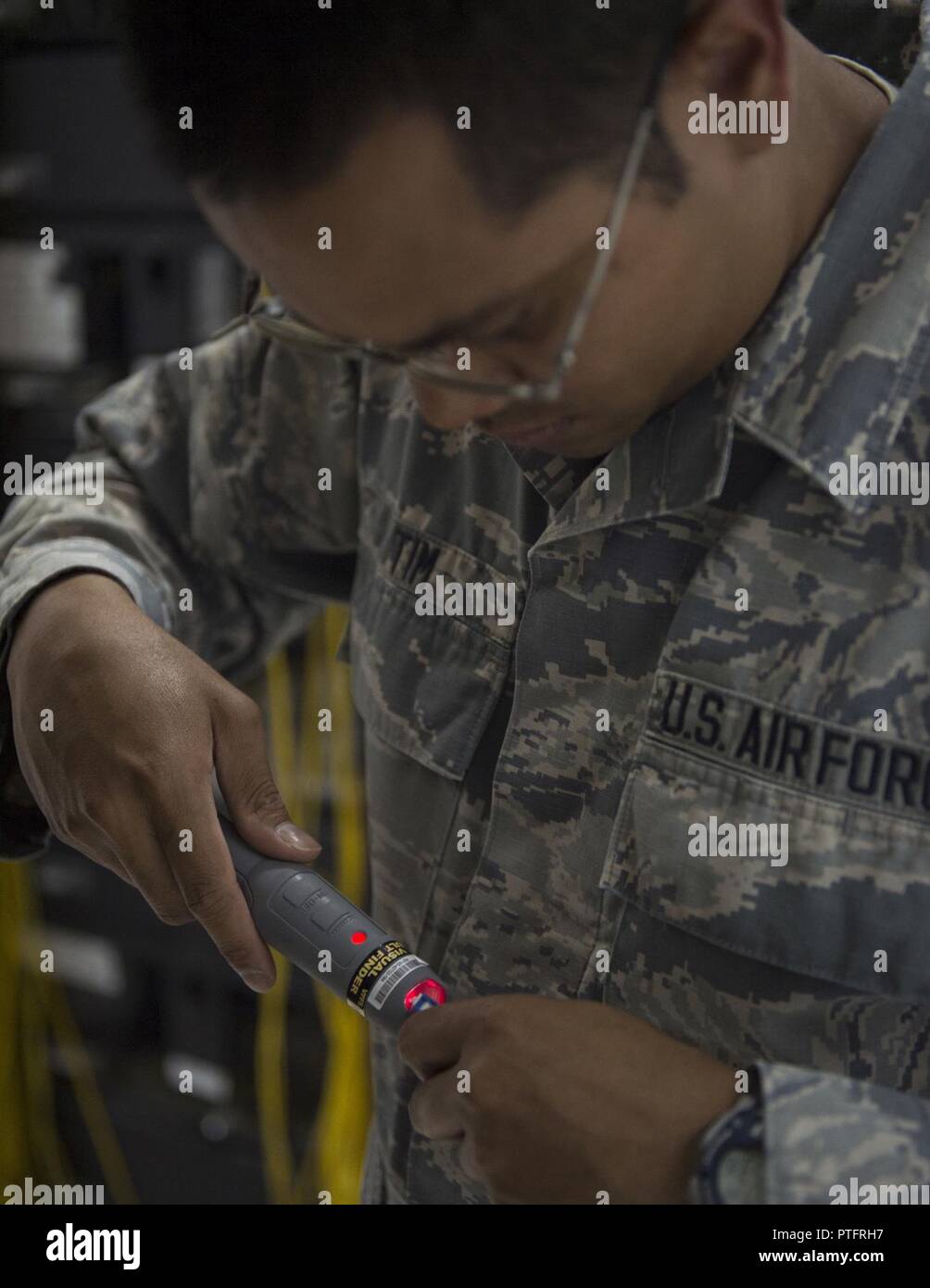 U.S. Air Force Senior Airman Monorom Tim, a network management technician with the 379th Expeditionary Communication Squadron, uses a visual fault finder to test the continuity of the fiber links at Al Udeid Air Base, Qatar, July 14, 2017. Tim is responsible for ensuring that the underlying infrastructure of the base network is operating within normal standards. Stock Photo