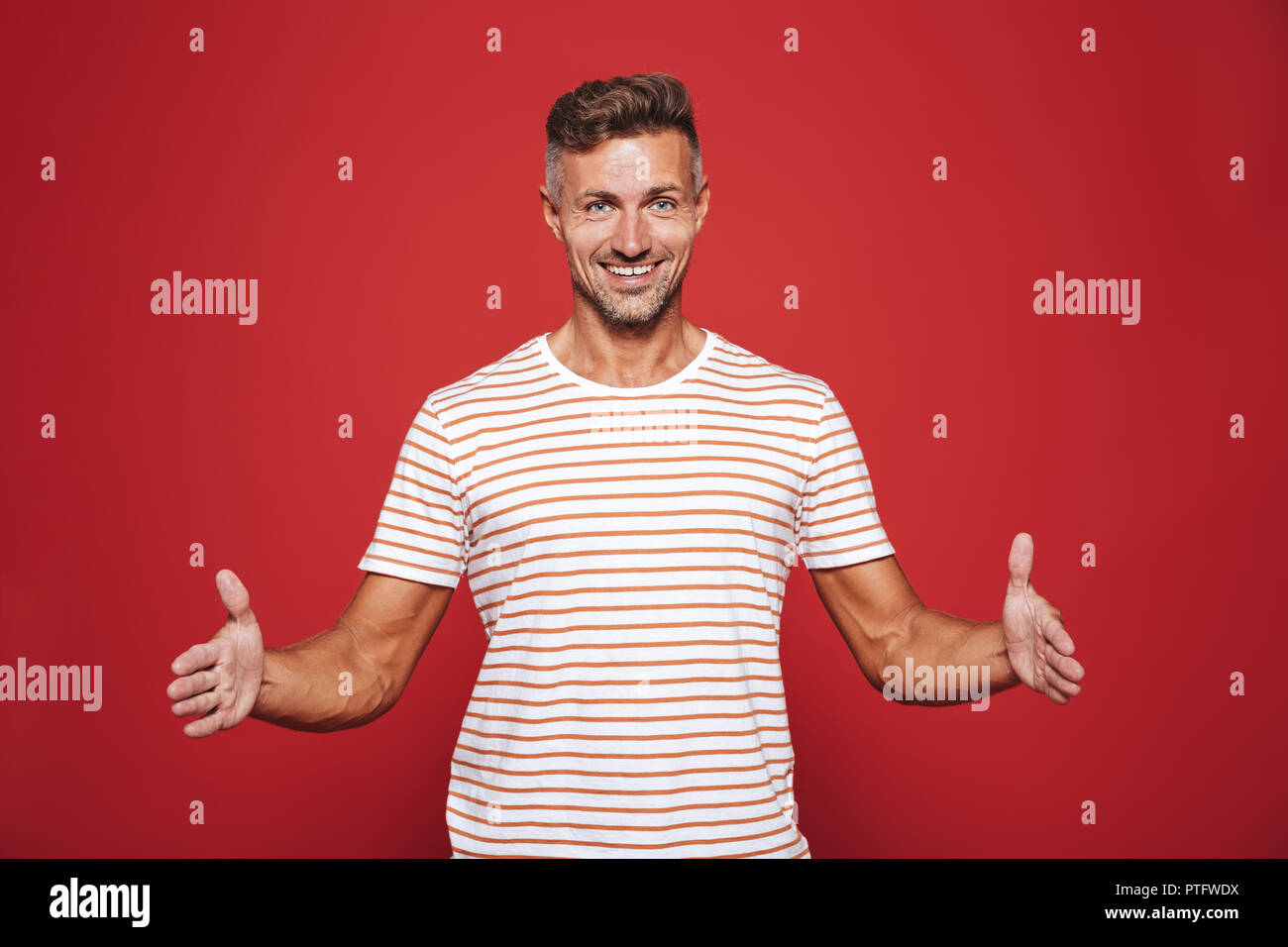 Successful man 30s in striped t-shirt gesturing and demonstrating size with copyspace isolated over red background Stock Photo