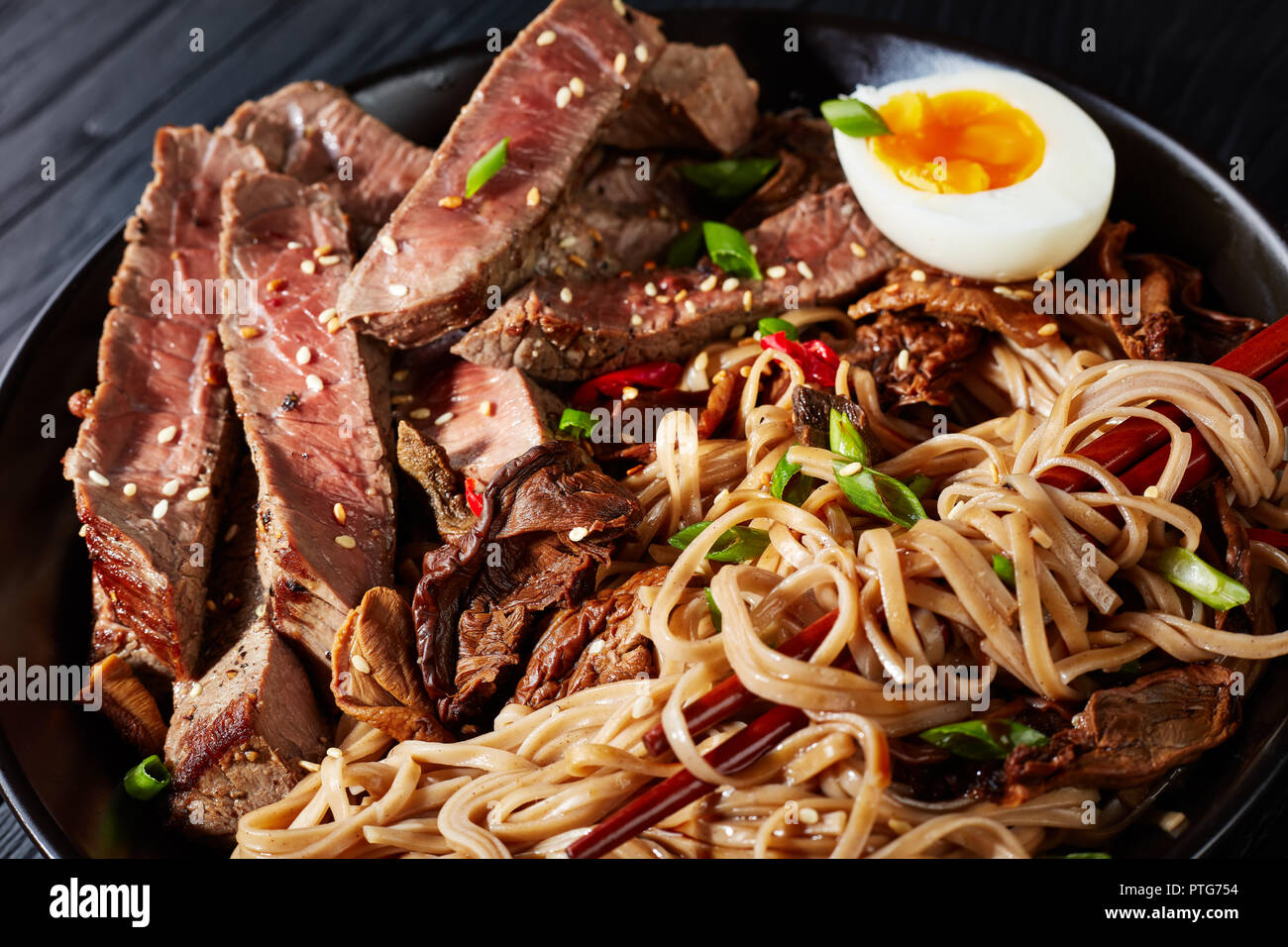 closeup of black bowl of Soba noodles with sliced roast beef, shiitake