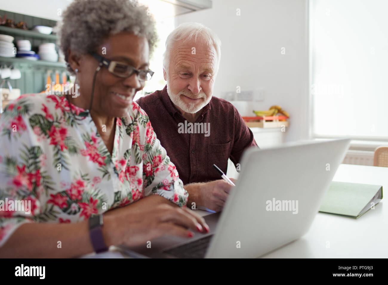 Senior couple paying bills at laptop in kitchen Stock Photo