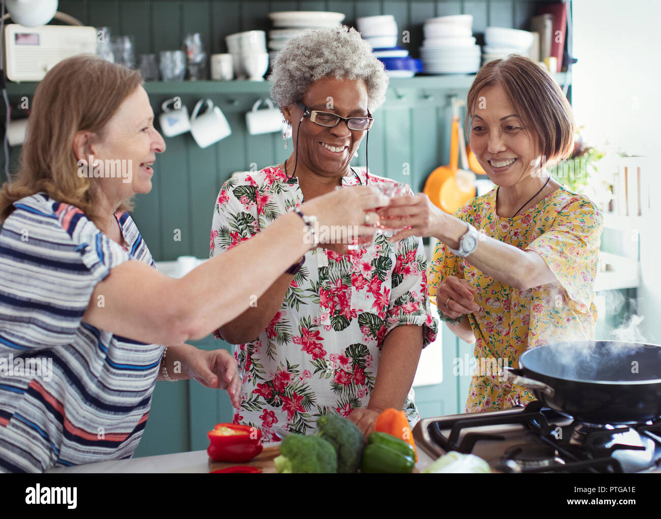 Active senior women friends cooking, toasting cocktails in kitchen Stock Photo