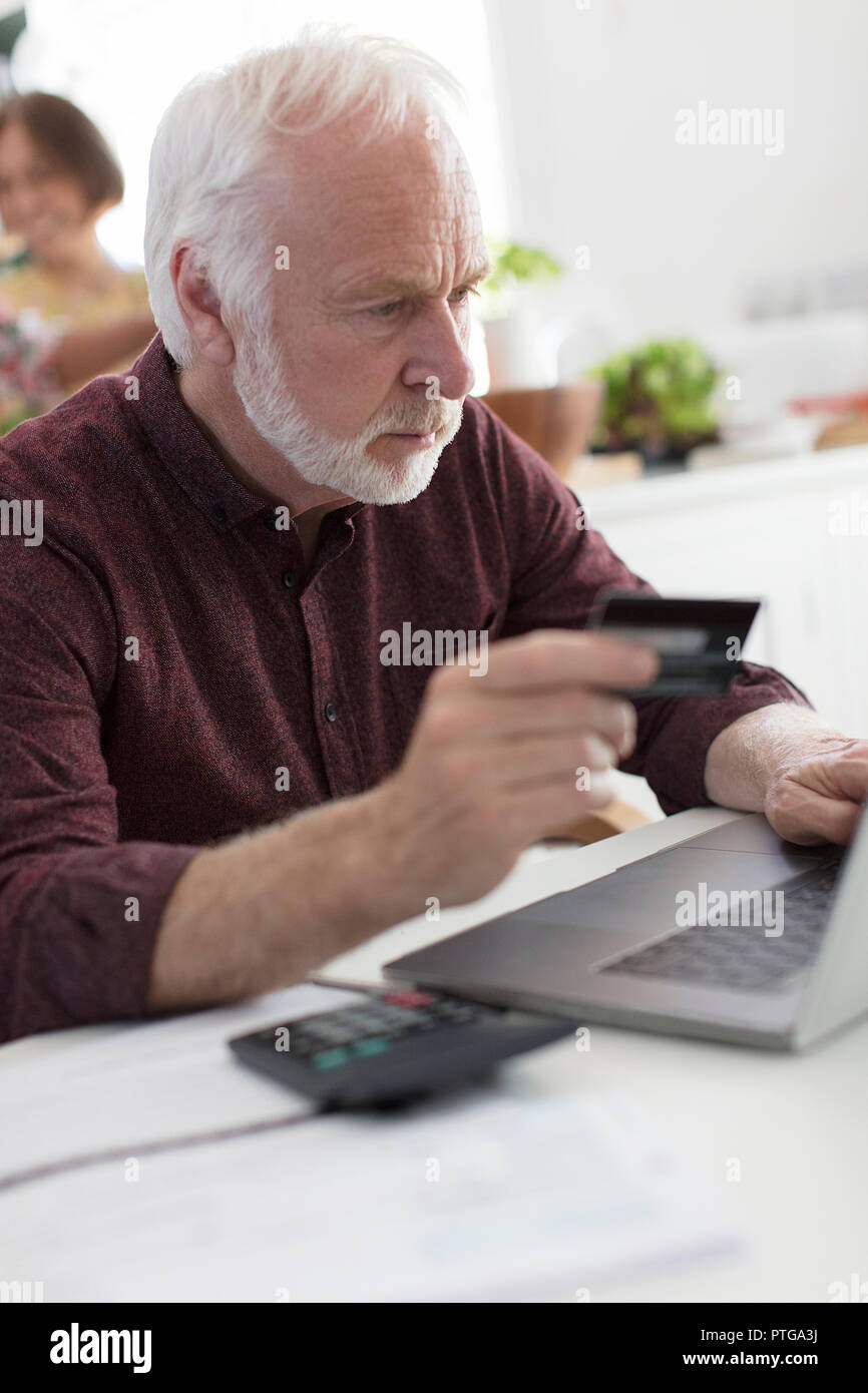Focused senior man with credit card paying bills at laptop Stock Photo