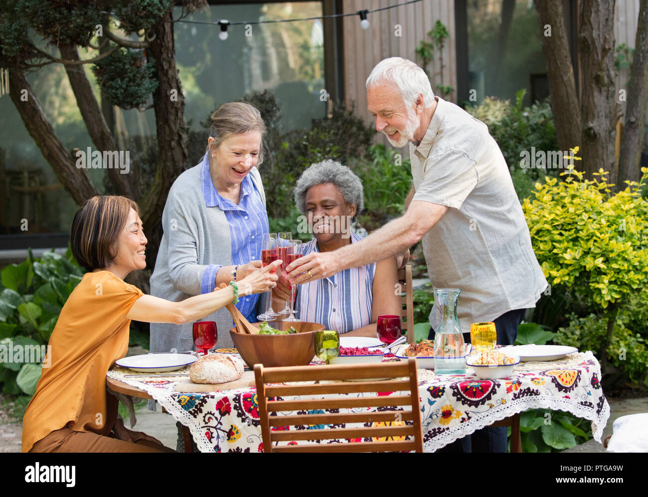 Active senior friends enjoying rose wine and lunch at patio table Stock Photo