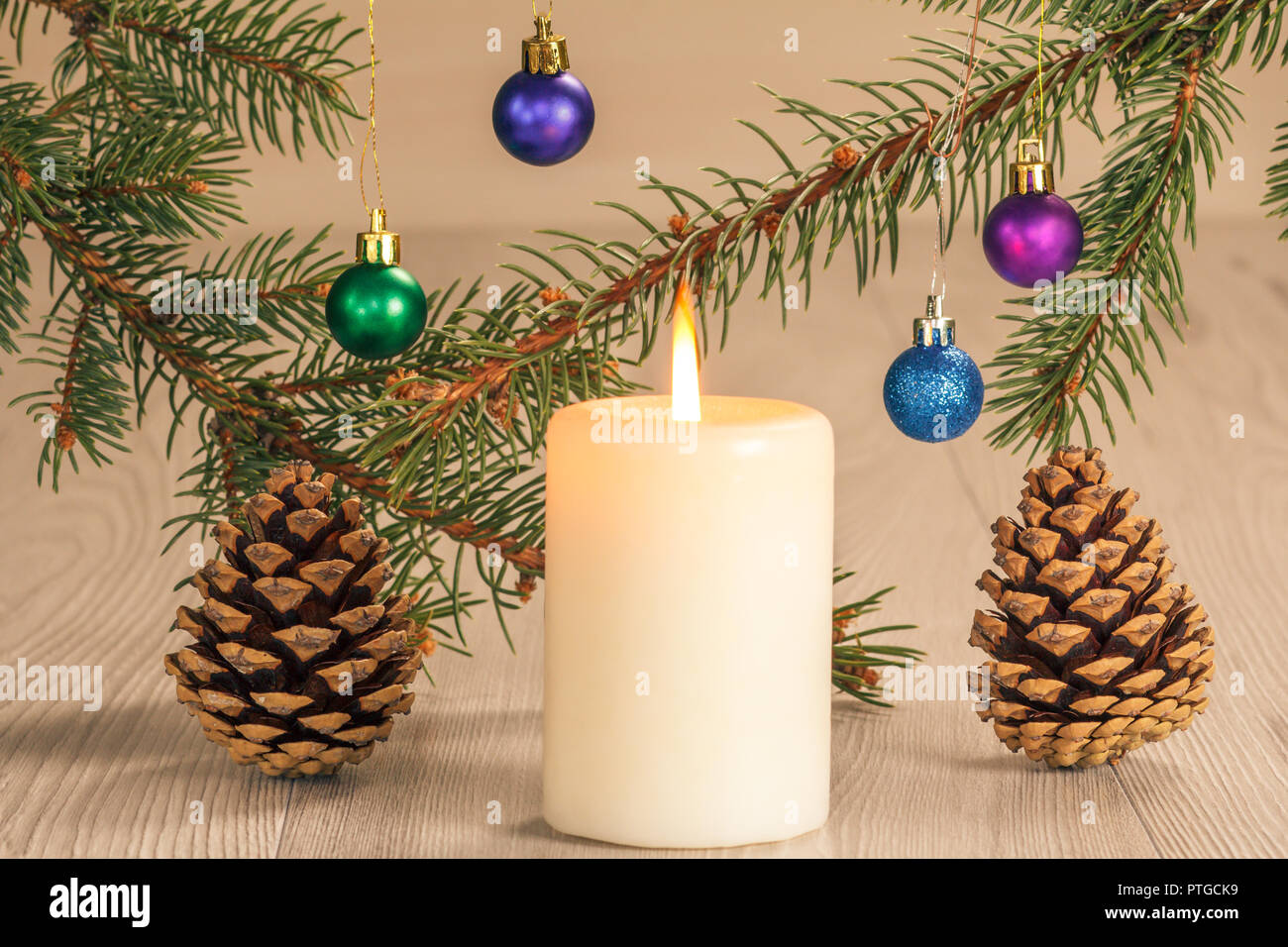White burning candle, natural fir tree branches with balls and cones on ...