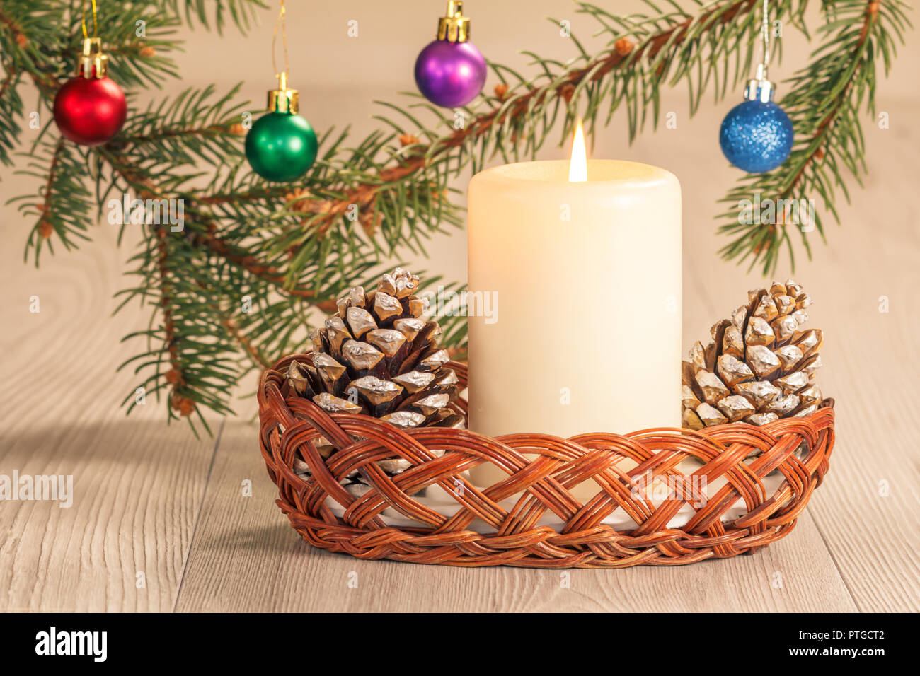 Burning candle, cones in wicker basket and natural fir tree branches ...