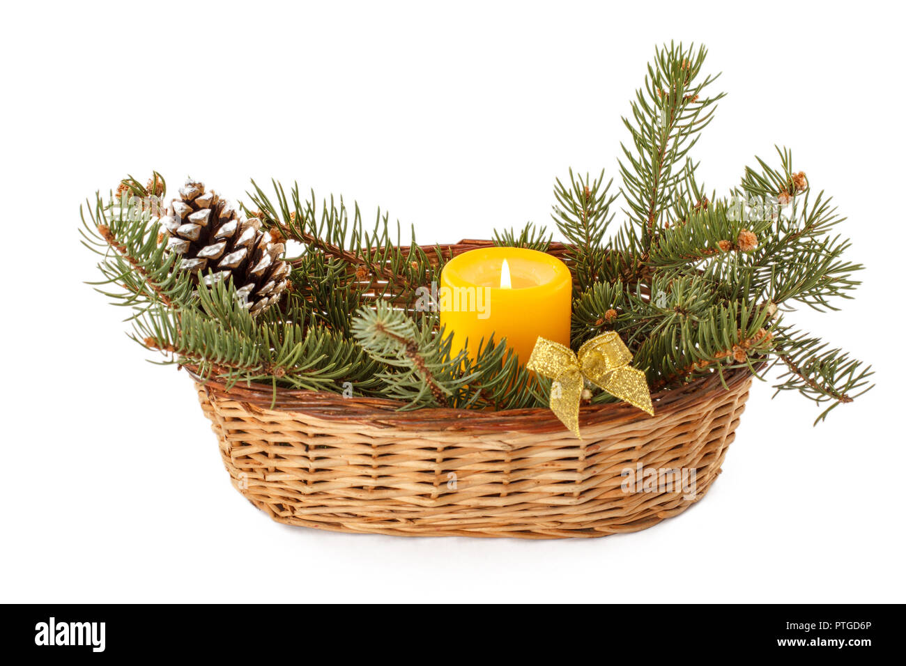Burning candle, cone and natural fir tree branches in wicker basket ...