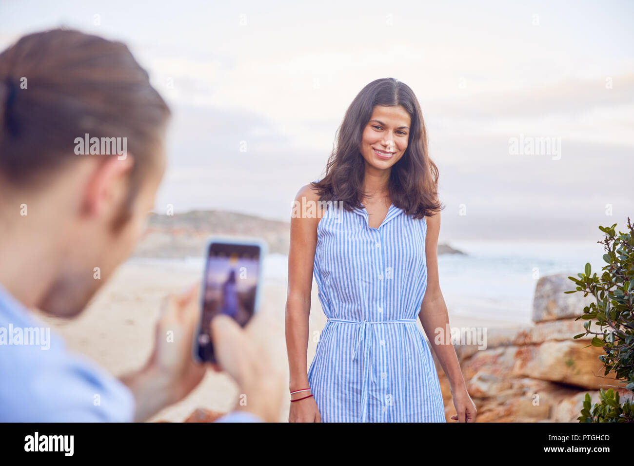 Young man with smart phone photographing girlfriend at beach Stock Photo