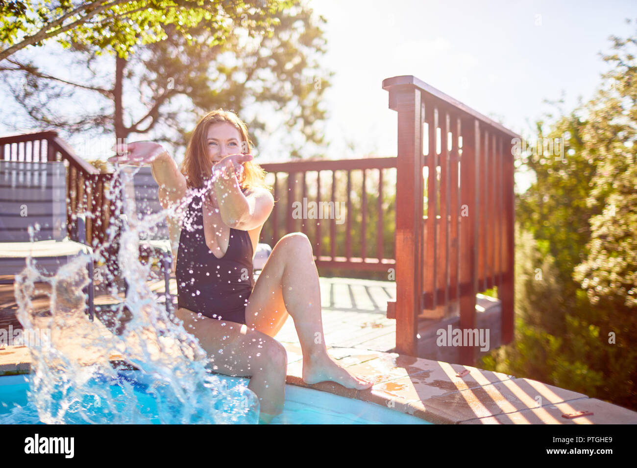 Playful young woman splashing water at sunny swimming pool Stock Photo