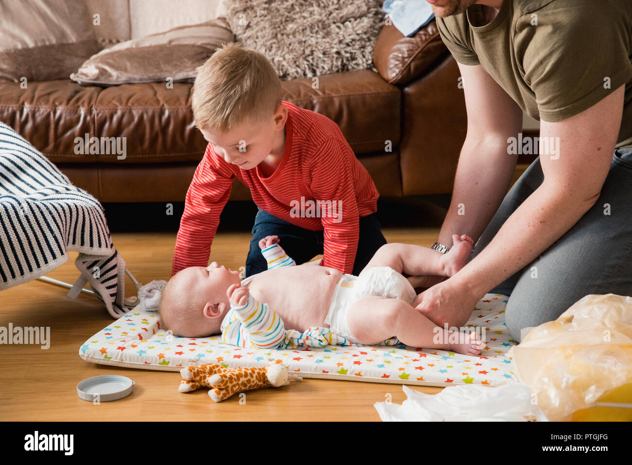 Little boy helping his father change his baby brother. They are both sitting on the floor in the living room. Stock Photo