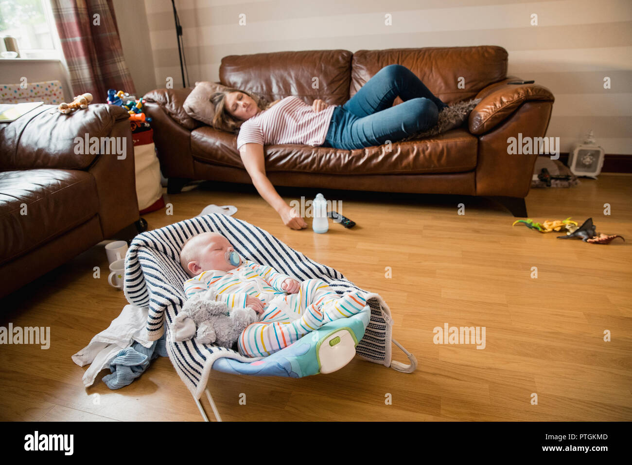 Exhausted mother having a nap on the sofa while her newborn child has a