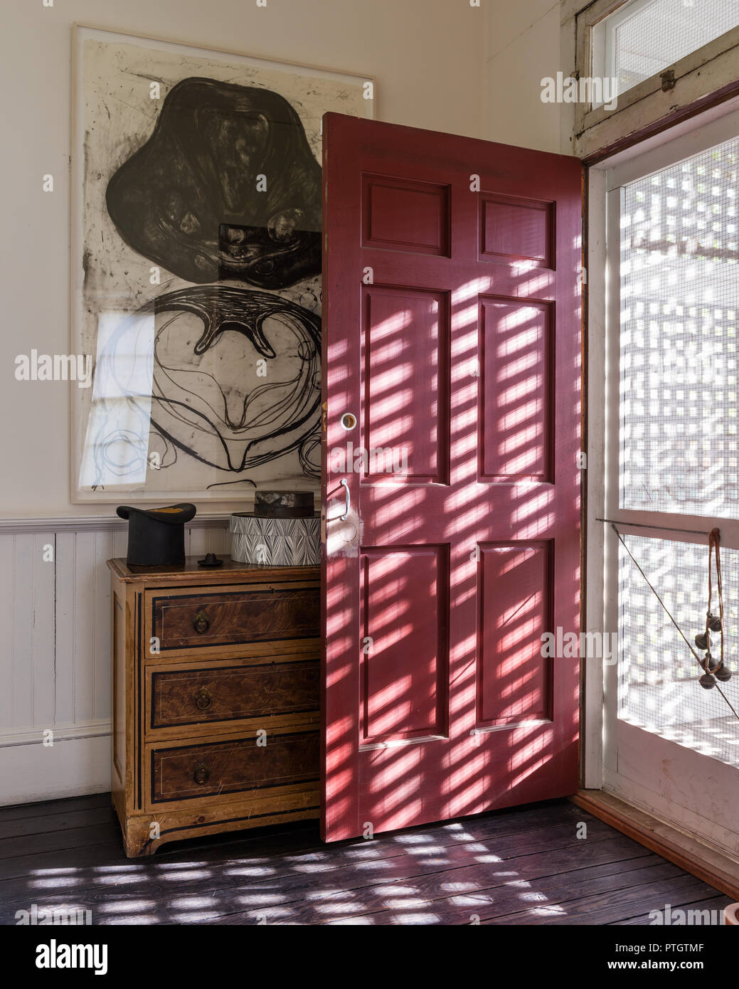 Lattice screen and mesh door with main door painted red. Small chest painted faux-bois 1870/80 American with artwork by Terry Winters. Stock Photo
