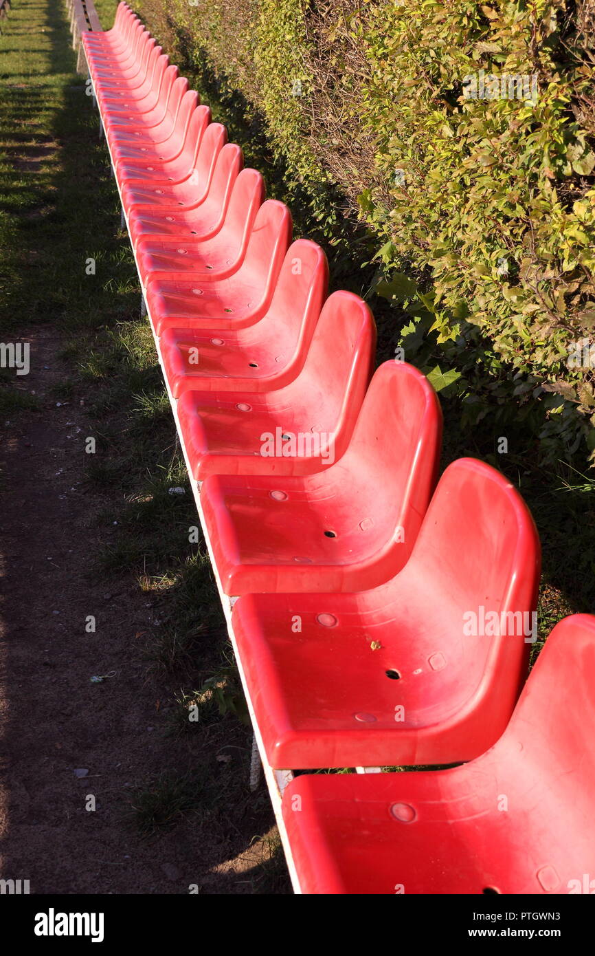 A row of small, red seats by the school's football pitch Stock Photo