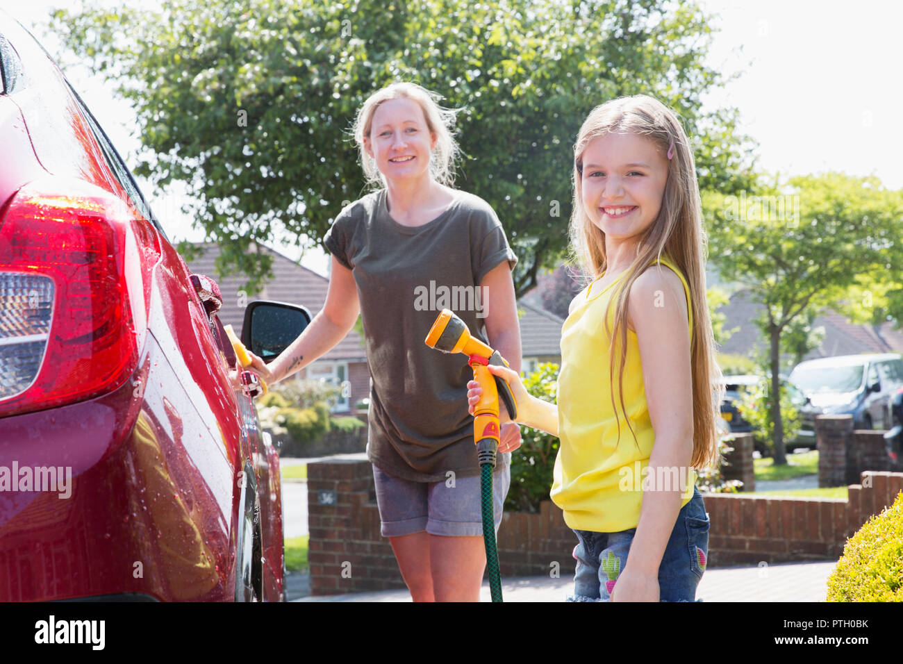 Portrait smiling mother and daughter washing car in sunny driveway Stock Photo