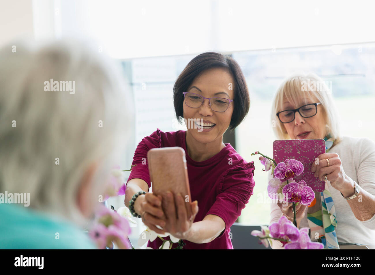 Active senior women with camera phone photographing orchids in flower arranging class Stock Photo