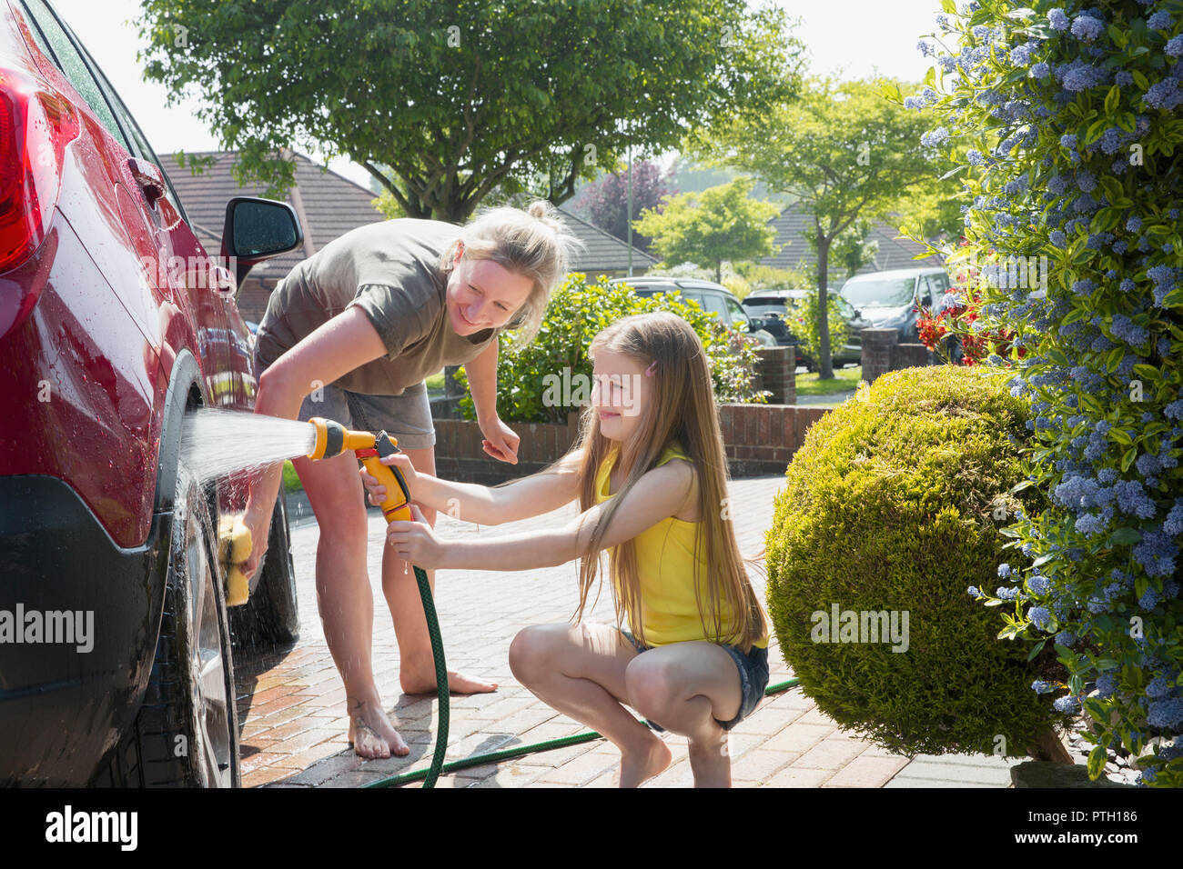 Mother and daughter washing car in sunny driveway Stock Photo