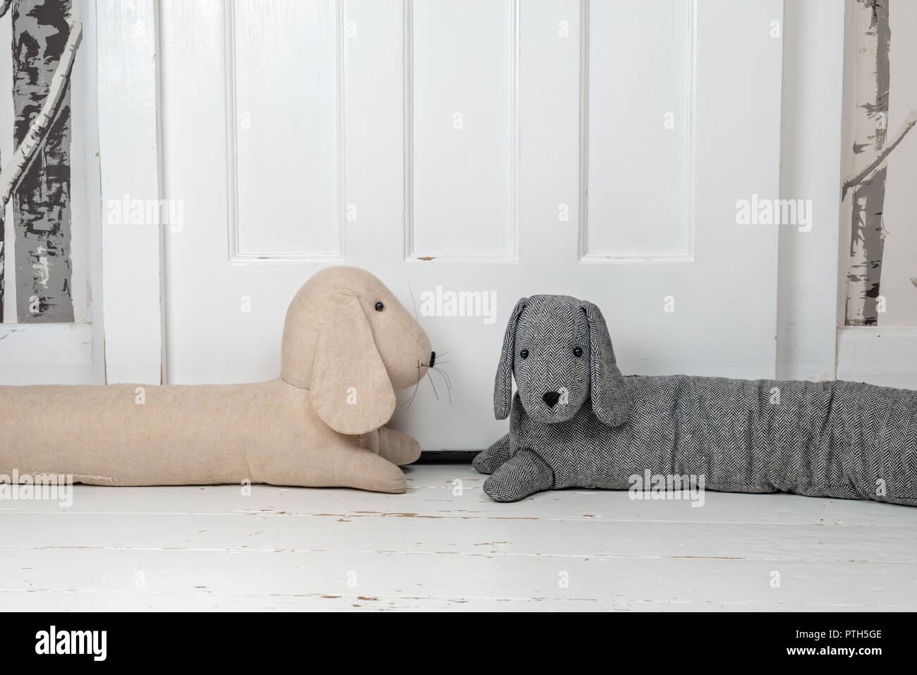 Two dog shaped draught excluders on a white painted wooden floor and in