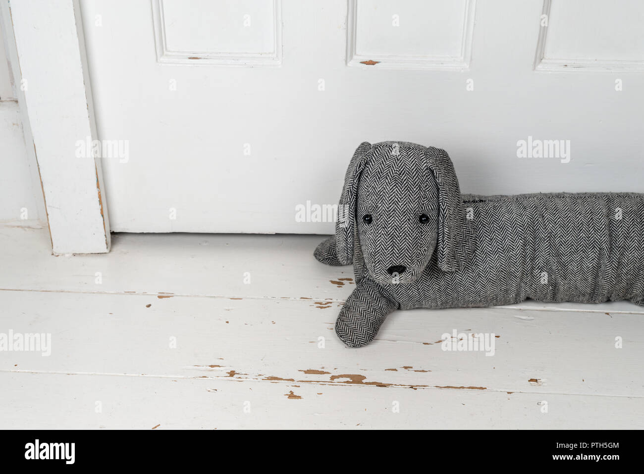Dog shaped draught excluder on a white painted wooden floor and in