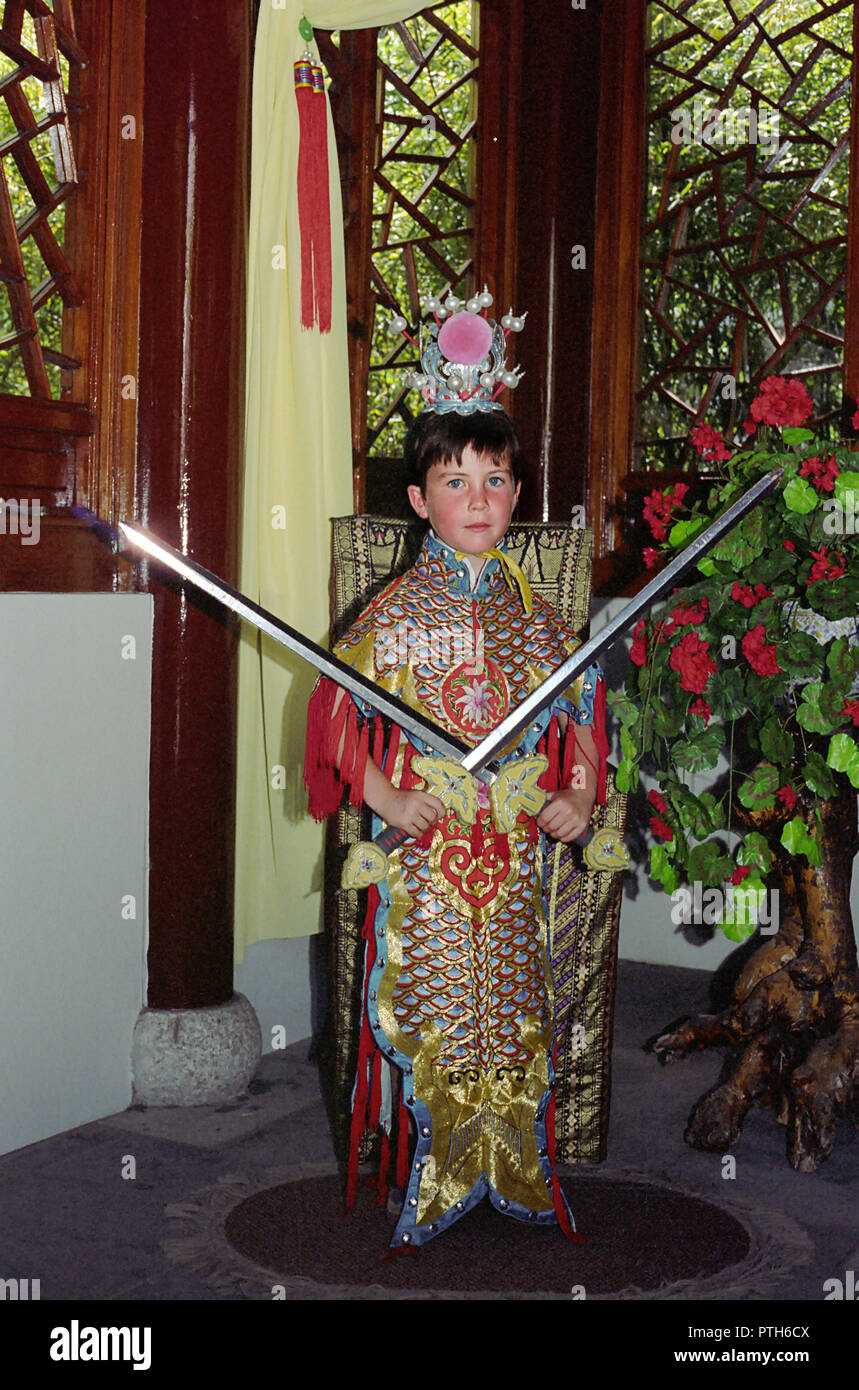 A five-year old boy dressed up in traditional Chinese costume with crossed swords, Chinese Garden of Friendship, Darling Harbour, Sydney, NSW, Australia.  MODEL RELEASED Stock Photo