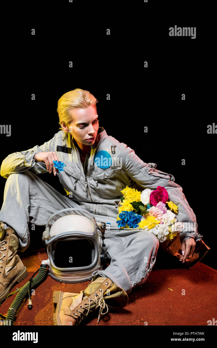 spacewoman in spacesuit with helmet and flowers in paper bag sitting on red planet Stock Photo