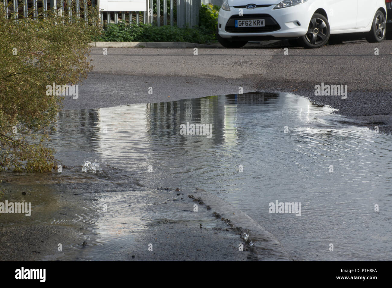 Burst water main leaking water onto road and pavement causing a flood Stock Photo