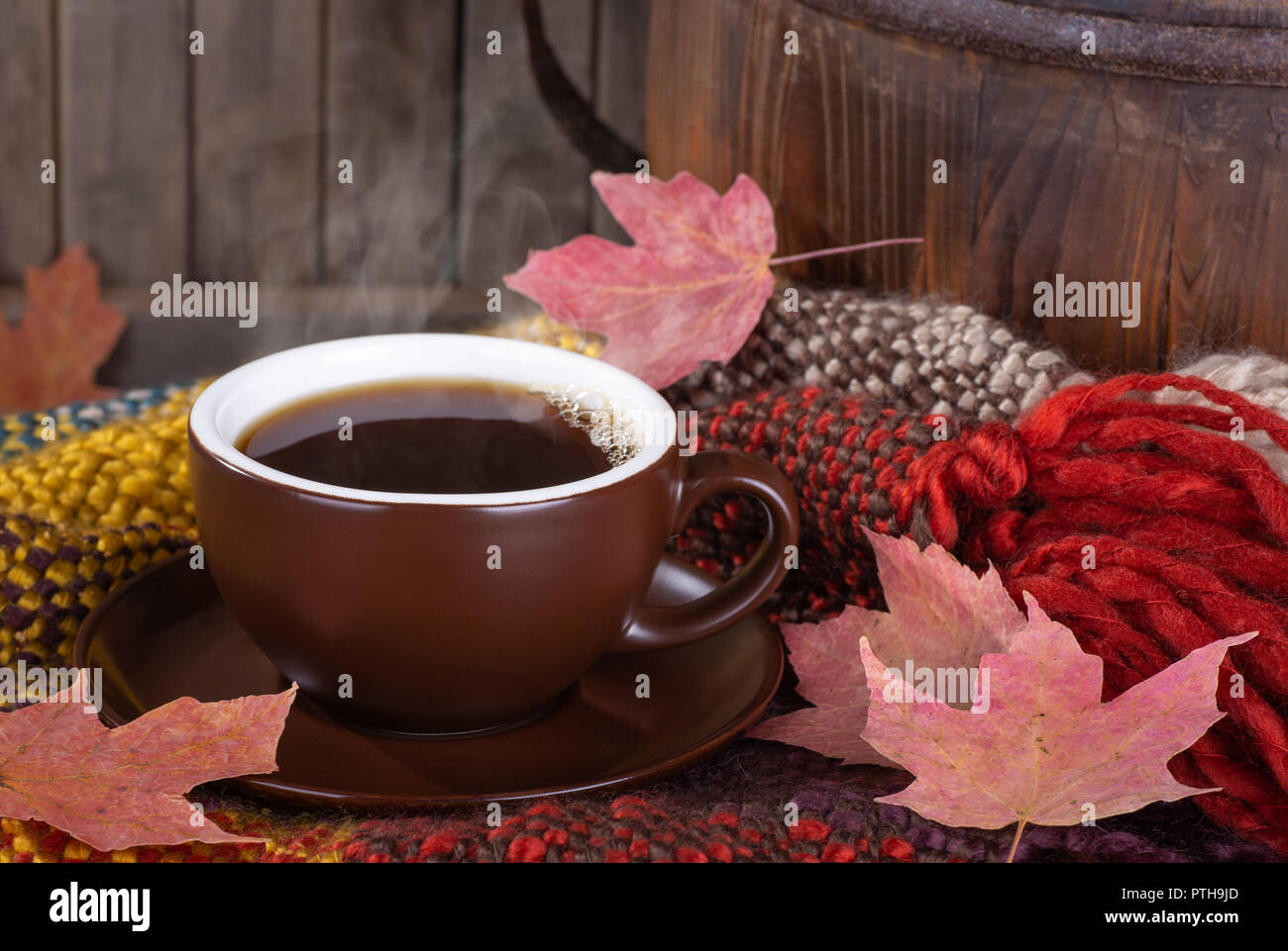 Steaming cup of coffee with autumn leaves on a colorful blanket Stock Photo