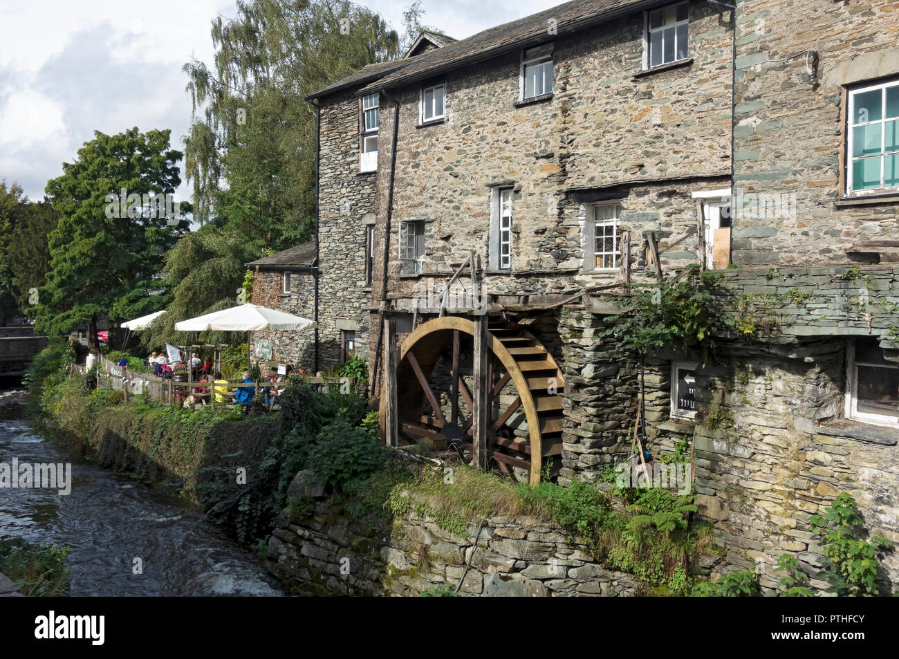 The Old Mill and and people sitting outside the Giggling Goose cafe in summer Ambleside Cumbria England UK United Kingdom GB Great Britain Stock Photo