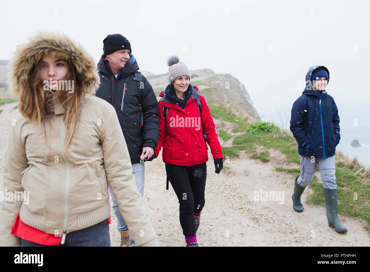 Family in warm clothing walking on snowy winter cliff path Stock Photo