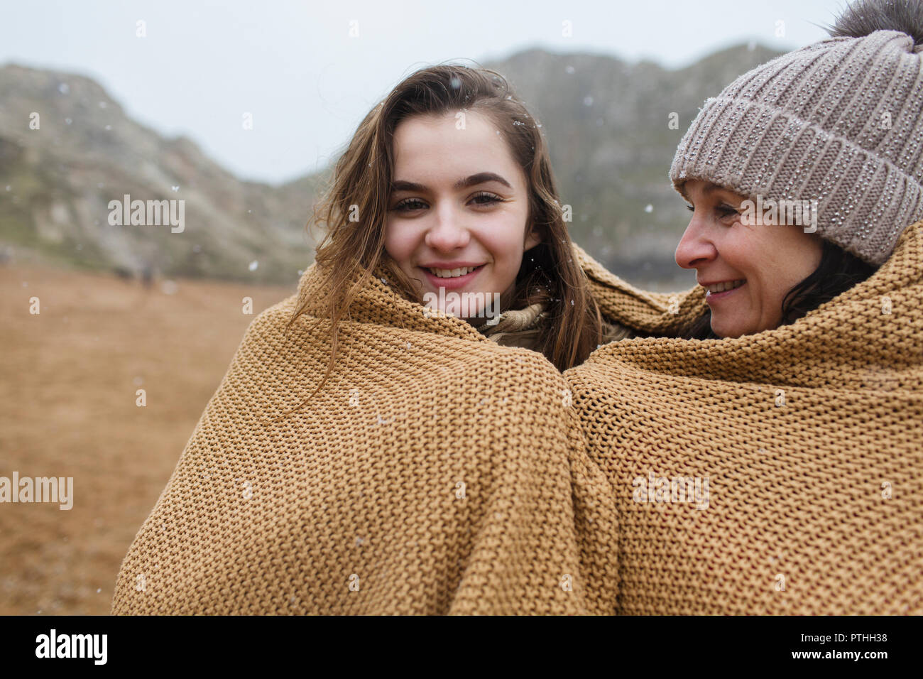 Portrait carefree mother and daughter wrapped in a blanket on snowy winter beach Stock Photo