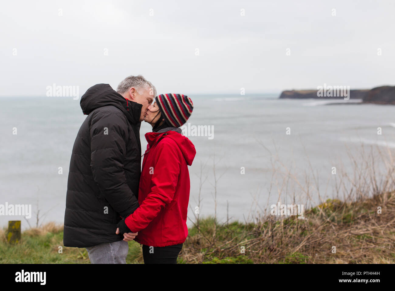 Affectionate couple kissing on cliff overlooking ocean Stock Photo
