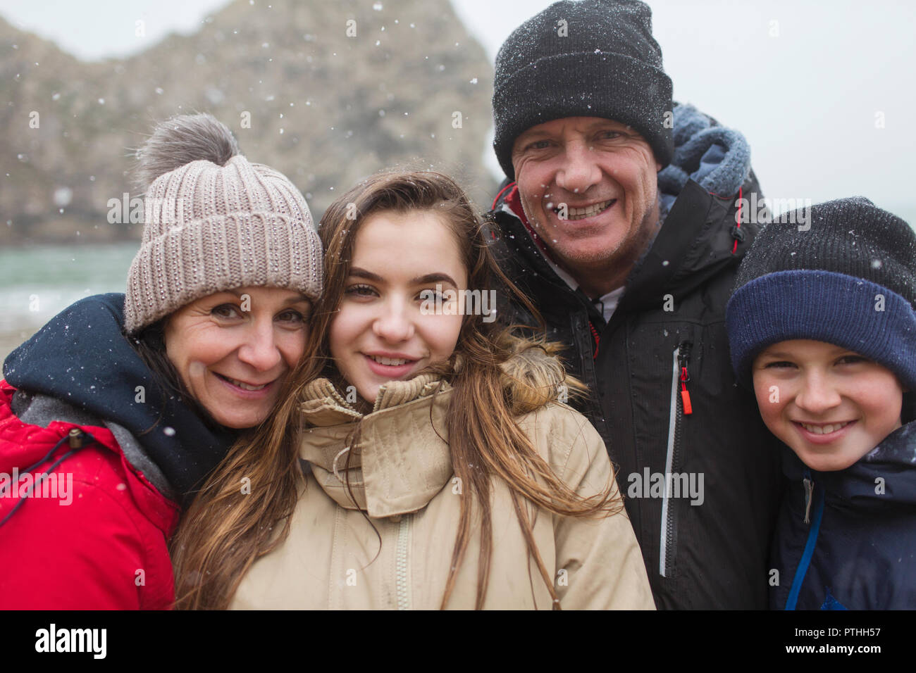 Snow falling over smiling family posing in warm clothing Stock Photo