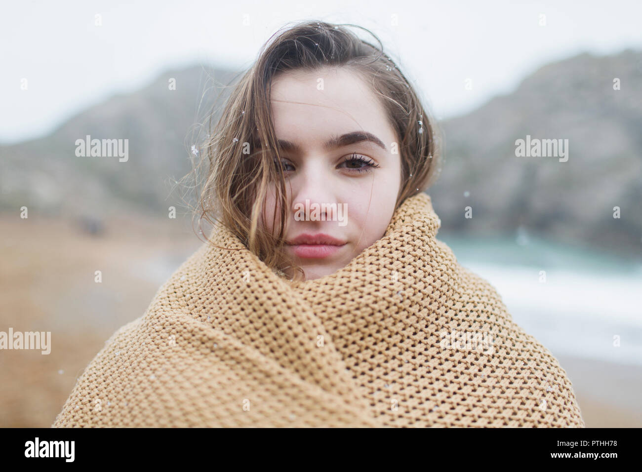 Portrait confident, serious girl with snow in hair wrapped in blanket on winter beach Stock Photo
