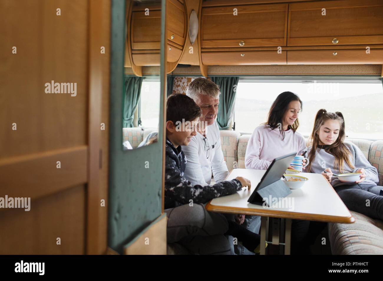 Family relaxing, eating and using digital tablet in motor home Stock Photo